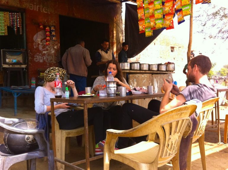 Enfield mieten in Indien: Westliche Touristen sitzen in einem Café am Strassnerand