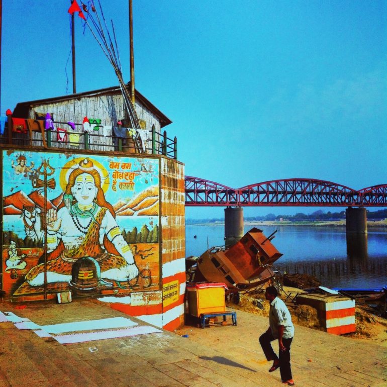 Mensch neben einem Shiva-Plakat am Ganges